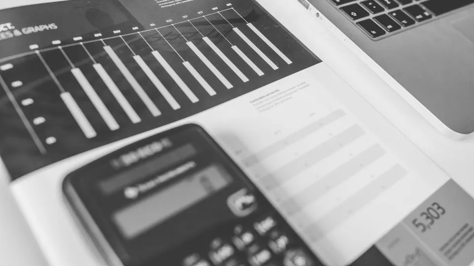 Calculator lying on printed bar charts next to a laptop
