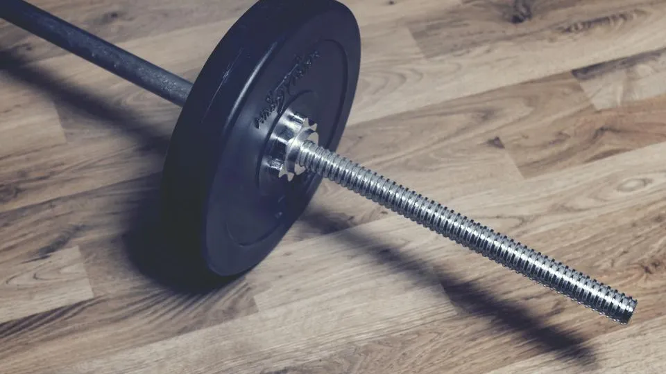 Barbell with a weight plate lying on a wooden gym floor