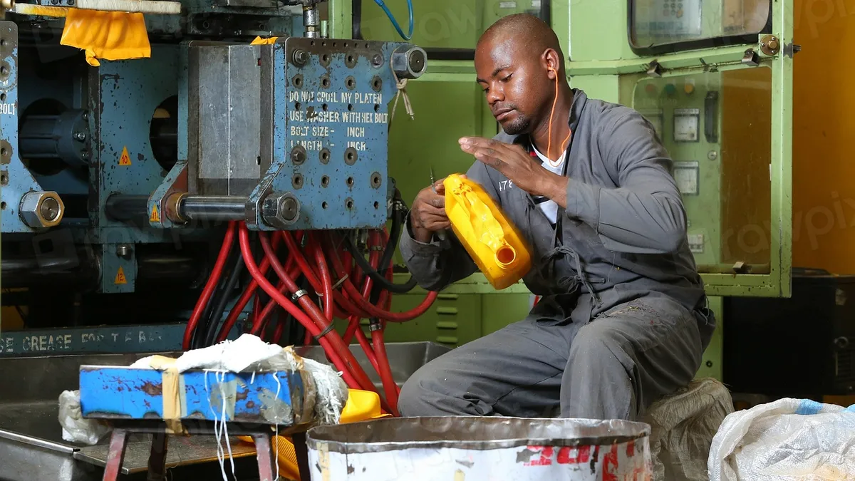 Worker inspecting a plastic product beside a moulding machine in a factory