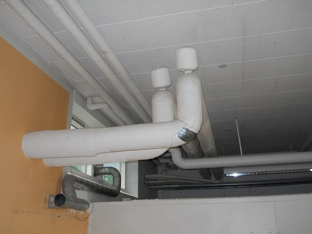 Ceiling pipes wrapped in thick white asbestos-fibre thermal insulation