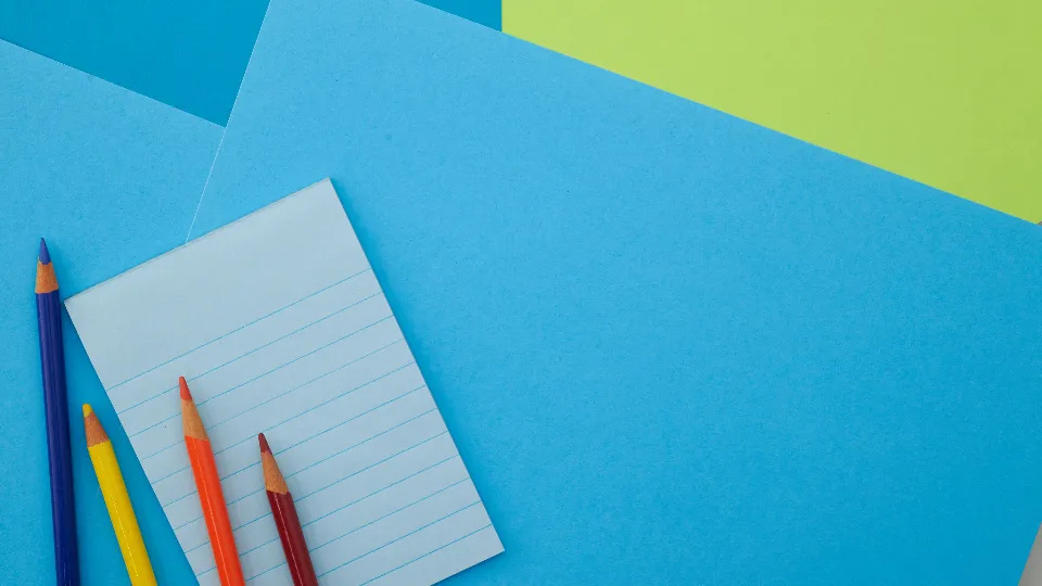 Coloured pencils and a lined notepad on blue and green paper
