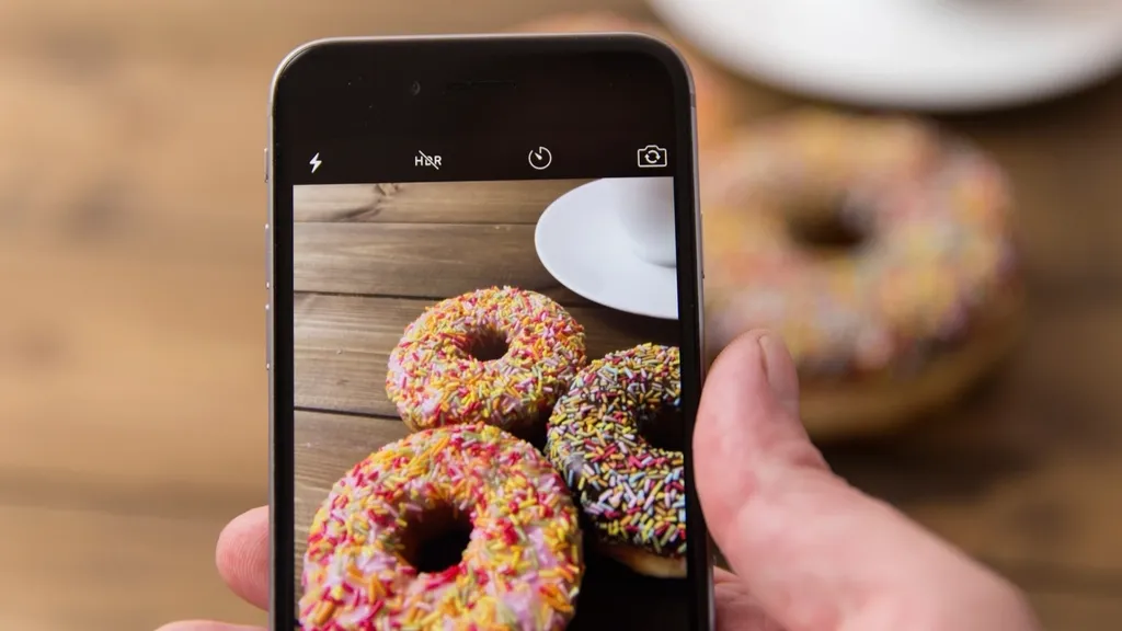 Hand holding a smartphone photographing doughnuts on a wooden table