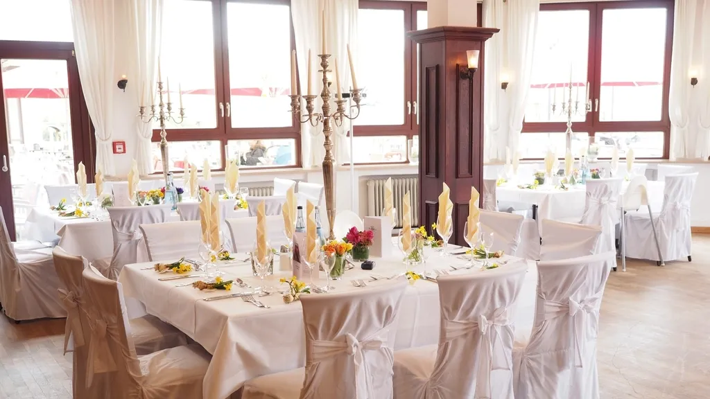 Banquet hall set for a wedding reception with white chairs and table settings