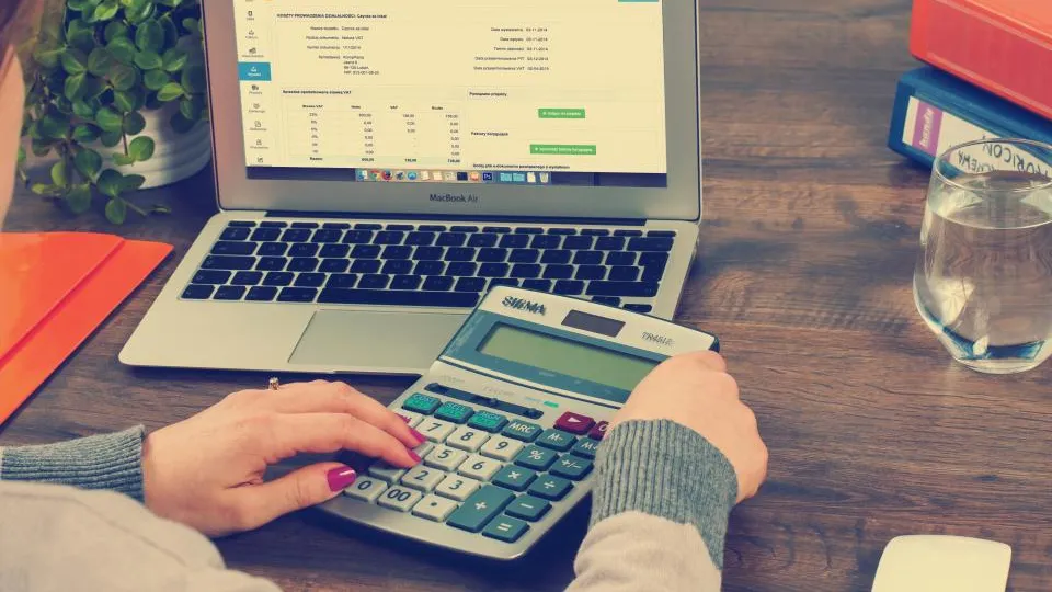 Person using a calculator in front of a laptop showing a spreadsheet