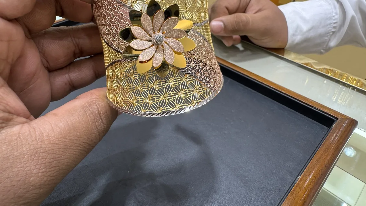 Hands holding a gold bracelet with a floral design over a jewelry shop counter