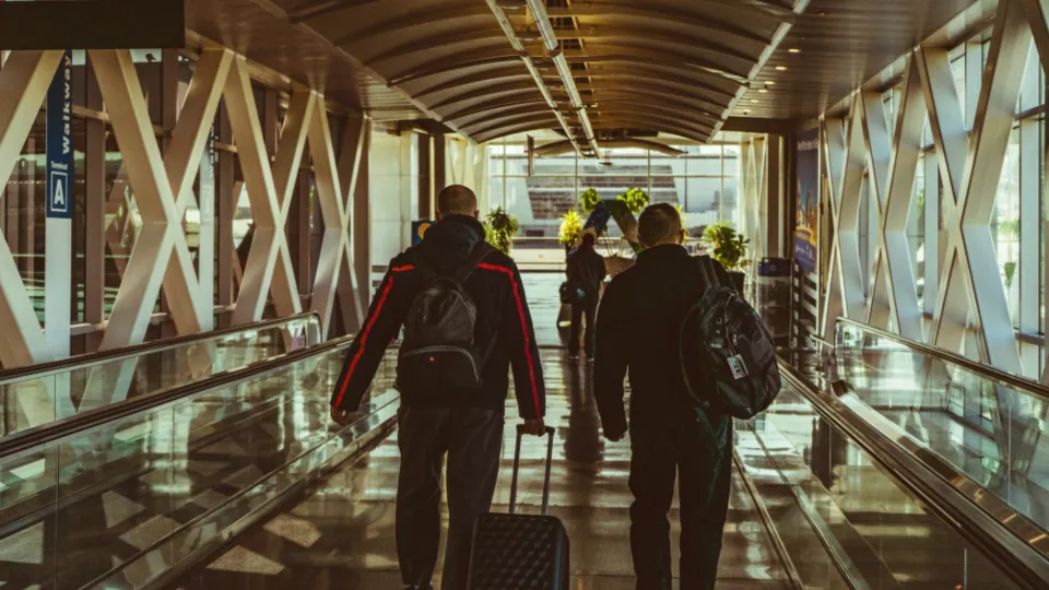 Two travellers with backpacks and luggage walking through an airport terminal