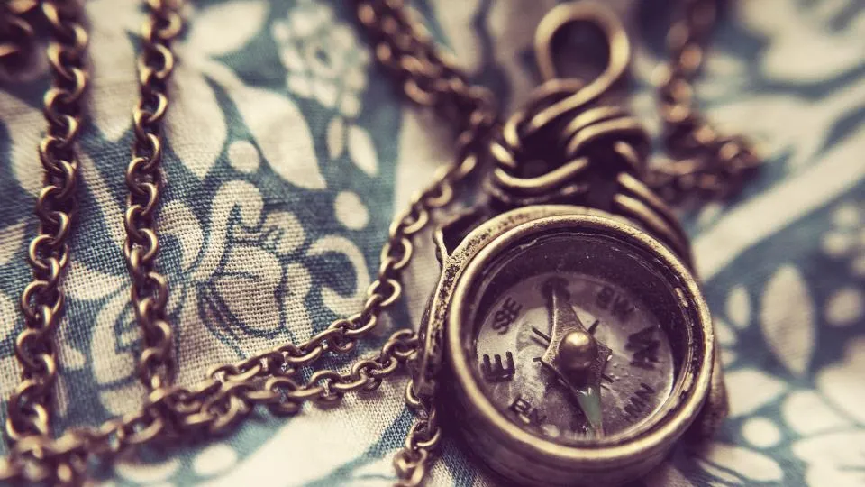 Antique pocket compass on a chain lying on patterned fabric
