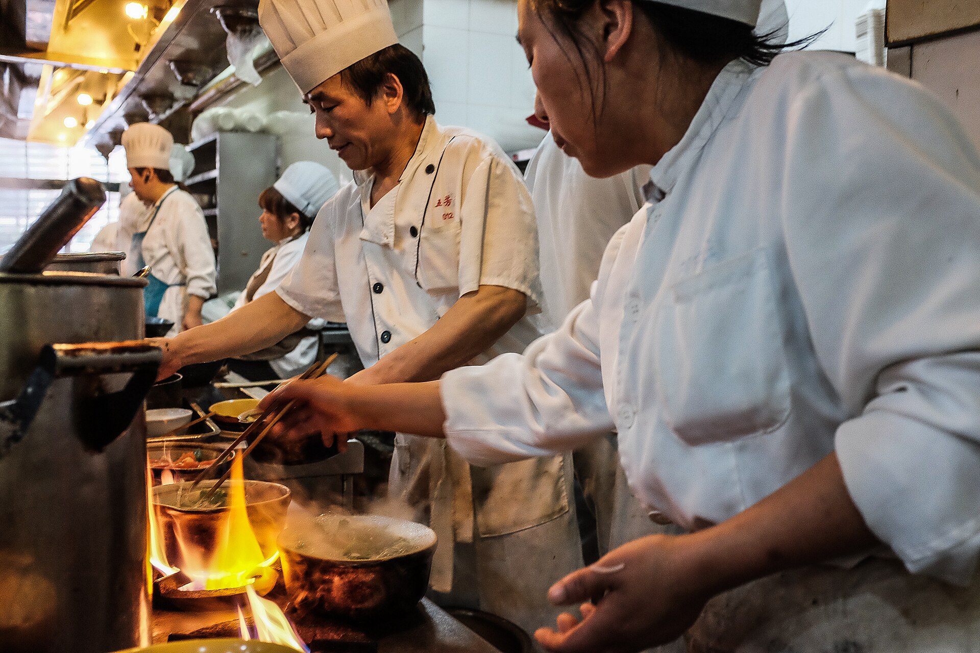 Several chefs working at once over flaming woks and pots in a busy restaurant kitchen