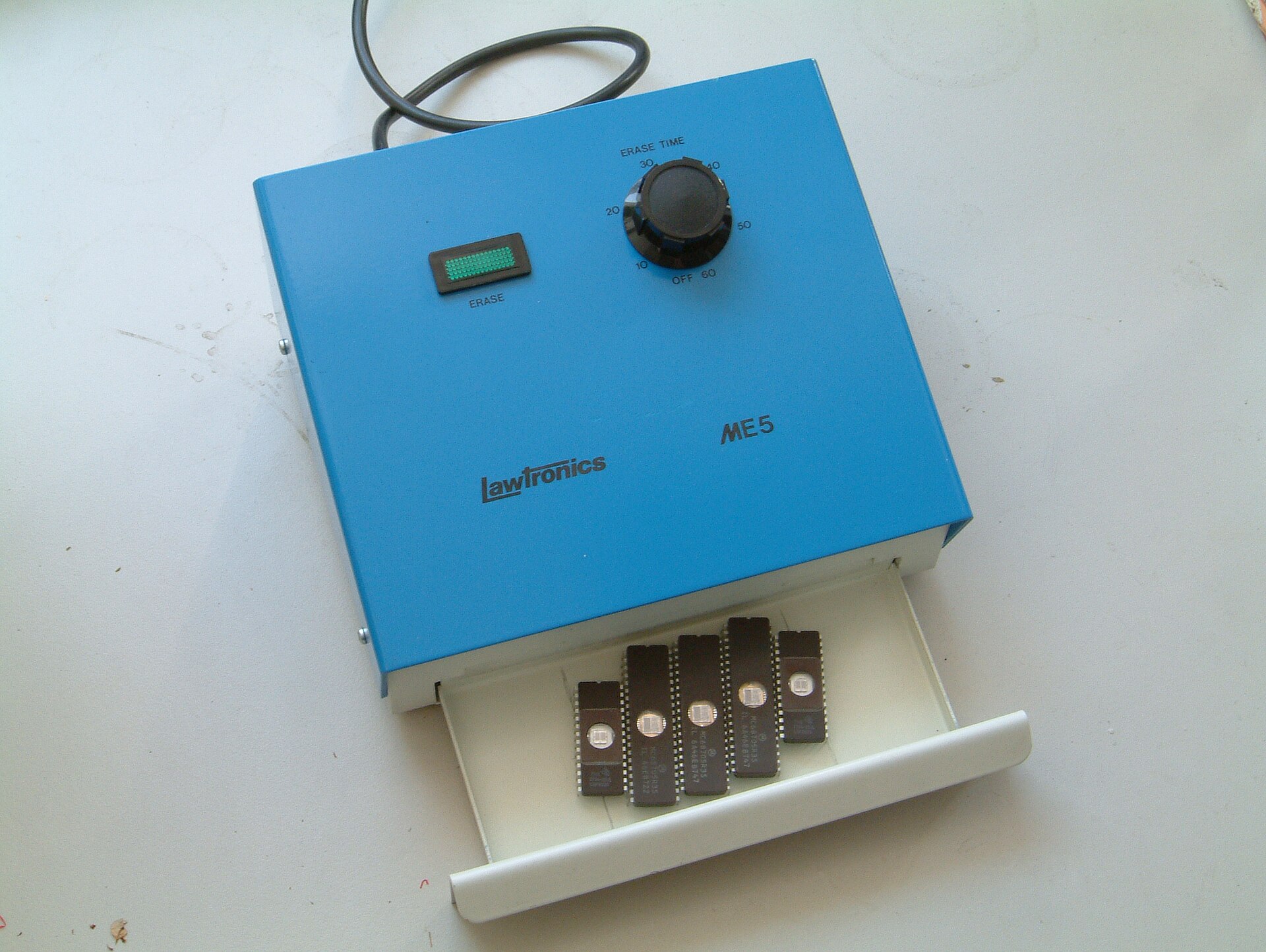 A blue UV EPROM eraser box with a timer dial and its drawer open, holding five EPROM chips.