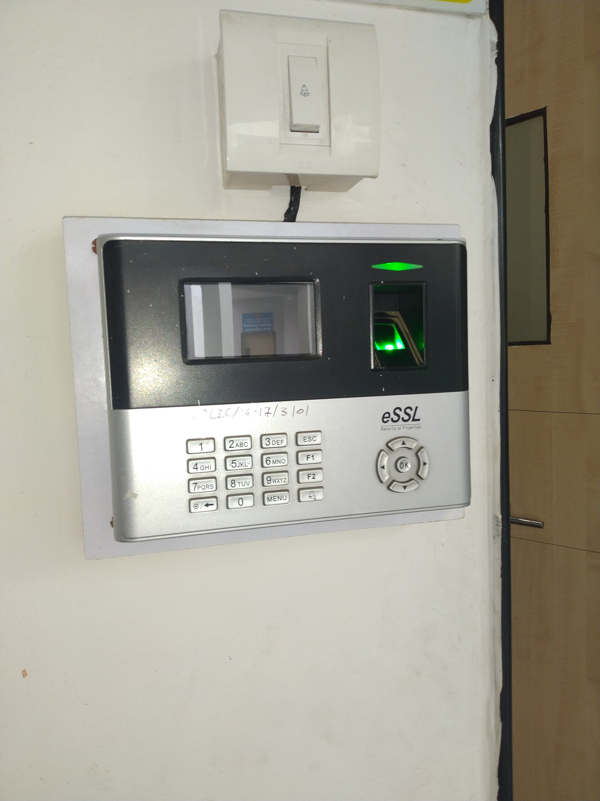 A wall-mounted fingerprint attendance terminal with a glowing green sensor and keypad