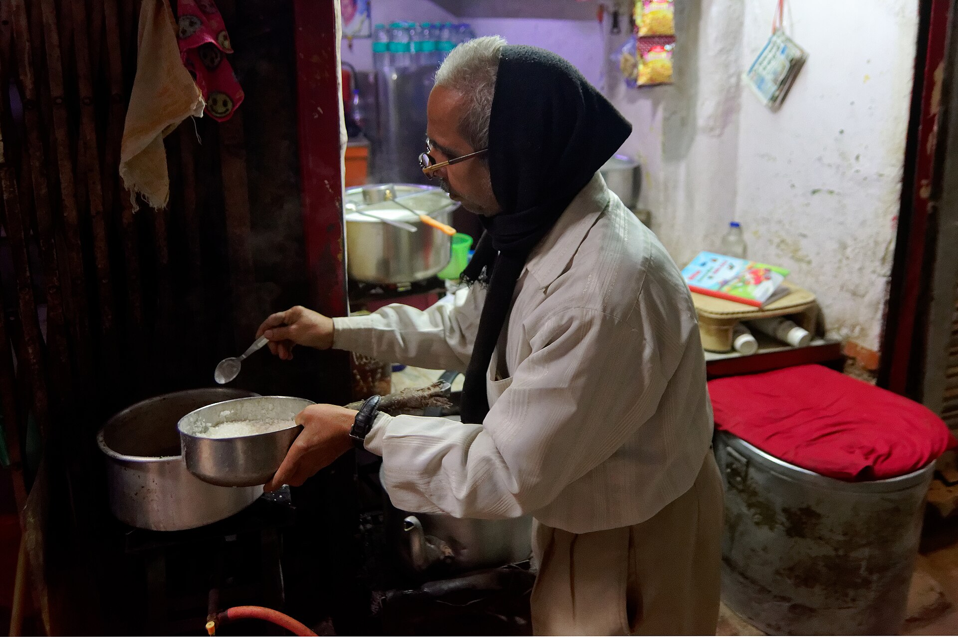 A tea seller adds sugar to a pot of milk tea simmering on a stove